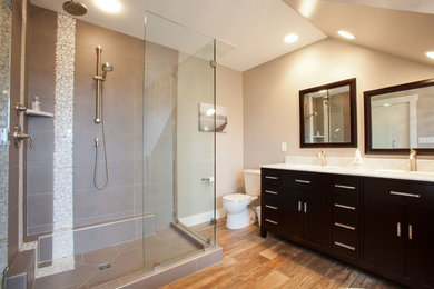 Inspiration for a medium sized classic ensuite bathroom in Vancouver with flat-panel cabinets, black cabinets, a freestanding bath, a corner shower, a one-piece toilet, grey walls, medium hardwood flooring, a submerged sink and granite worktops.