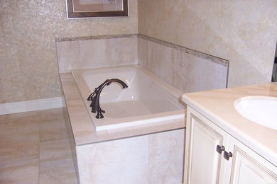 Example of a master porcelain tile porcelain tile corner bathtub design in Toronto with an undermount sink, furniture-like cabinets, white cabinets, quartz countertops, a one-piece toilet and beige walls