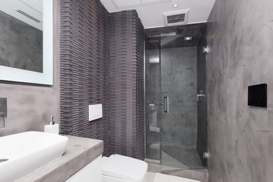 Ejemplo de cuarto de baño contemporáneo pequeño con armarios con paneles lisos, puertas de armario de madera clara, encimera de cemento, ducha esquinera, sanitario de pared, baldosas y/o azulejos negros, baldosas y/o azulejos de cemento y aseo y ducha