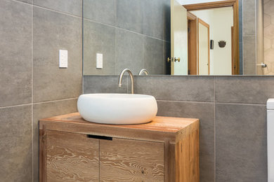Small modern ensuite bathroom in Christchurch with freestanding cabinets, medium wood cabinets, a walk-in shower, a one-piece toilet, grey tiles, ceramic tiles, grey walls, a trough sink and wooden worktops.