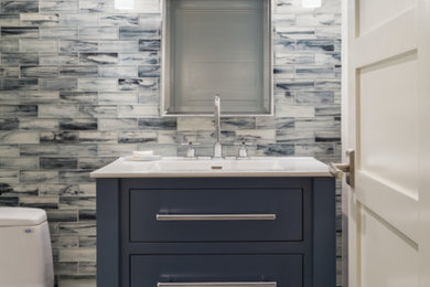Example of a small trendy blue tile, gray tile, white tile and porcelain tile porcelain tile and beige floor bathroom design in Providence with flat-panel cabinets, blue cabinets, a one-piece toilet, an integrated sink, solid surface countertops and white countertops