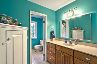 Example of a classic master ceramic tile bathroom design in Baltimore with an integrated sink, furniture-like cabinets, medium tone wood cabinets, solid surface countertops, a one-piece toilet and blue walls