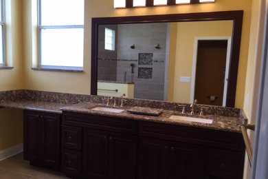 Example of a mid-sized transitional 3/4 limestone floor and beige floor bathroom design in Tampa with recessed-panel cabinets, brown cabinets, yellow walls, an undermount sink and granite countertops