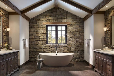 Photo of a large rustic bathroom in Other with beaded cabinets, dark wood cabinets, a freestanding bath, brown tiles, stone tiles, white walls, dark hardwood flooring, a submerged sink, limestone worktops and brown floors.