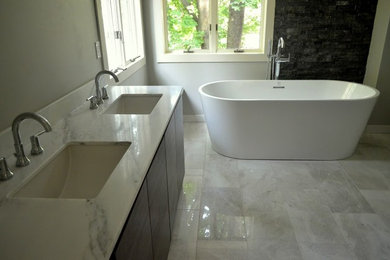 Diseño de cuarto de baño principal actual con bañera exenta, paredes grises, suelo de mármol, lavabo bajoencimera, encimera de mármol, armarios con paneles lisos y puertas de armario de madera en tonos medios