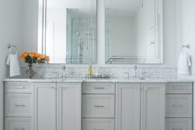 На фото: большая главная ванная комната в стиле неоклассика (современная классика) с фасадами с утопленной филенкой, душем в нише, унитазом-моноблоком, белой плиткой, стеклянной плиткой, белыми стенами, мраморным полом, врезной раковиной, мраморной столешницей, белым полом, душем с распашными дверями и серыми фасадами