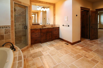 Inspiration for a large rustic master beige tile and stone tile travertine floor drop-in bathtub remodel in Other with flat-panel cabinets, dark wood cabinets, a two-piece toilet, beige walls, an undermount sink and granite countertops