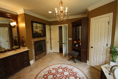 他の地域にある広いトラディショナルスタイルのおしゃれなマスターバスルーム (濃色木目調キャビネット、茶色い壁、トラバーチンの床、アンダーカウンター洗面器) の写真
