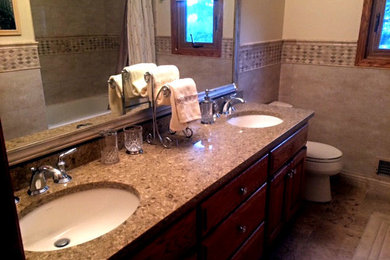 ミネアポリスにある高級な広いトラディショナルスタイルのおしゃれなマスターバスルーム (オーバーカウンターシンク、レイズドパネル扉のキャビネット、濃色木目調キャビネット、クオーツストーンの洗面台、一体型トイレ	、ベージュの壁、セラミックタイルの床、アルコーブ型浴槽、シャワー付き浴槽	、ベージュのタイル、磁器タイル) の写真