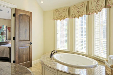 Example of a mid-sized transitional master limestone floor drop-in bathtub design in Atlanta with beige walls, white cabinets and granite countertops