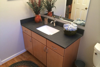 Inspiration for a mid-sized timeless 3/4 black tile and stone slab medium tone wood floor bathroom remodel in Richmond with flat-panel cabinets, medium tone wood cabinets, a two-piece toilet, gray walls, an undermount sink and solid surface countertops