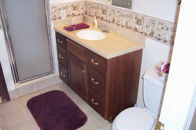 Mid-sized beige tile corner shower photo in New York with a drop-in sink, raised-panel cabinets, medium tone wood cabinets, a one-piece toilet and white walls