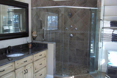 Example of a mid-sized arts and crafts master beige tile and stone tile ceramic tile and brown floor corner shower design in Boston with an undermount sink, raised-panel cabinets, light wood cabinets, granite countertops, a one-piece toilet, white walls and a hinged shower door