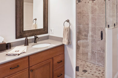 Example of a transitional master beige tile, brown tile and ceramic tile ceramic tile and gray floor alcove shower design in Other with raised-panel cabinets, medium tone wood cabinets, beige walls, an undermount sink, quartz countertops and a hinged shower door
