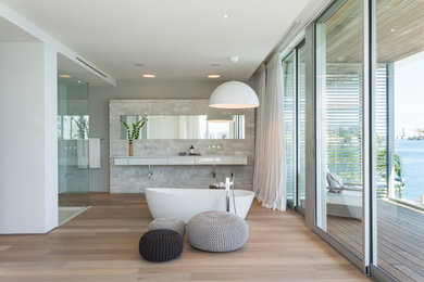 Großes Modernes Badezimmer En Suite mit flächenbündigen Schrankfronten, weißen Schränken, freistehender Badewanne, hellem Holzboden, weißer Wandfarbe und braunem Boden in Miami