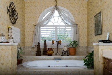 ローリーにあるお手頃価格の中くらいなトラディショナルスタイルのおしゃれなマスターバスルーム (レイズドパネル扉のキャビネット、中間色木目調キャビネット、大理石の洗面台、ドロップイン型浴槽、ベージュのタイル、セラミックタイル、茶色い壁) の写真