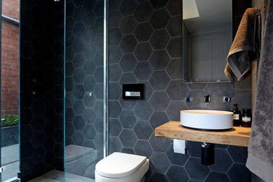 Bathroom - mid-sized modern 3/4 black tile and marble tile concrete floor and gray floor bathroom idea in Orange County with open cabinets, light wood cabinets, a one-piece toilet, black walls, a vessel sink and wood countertops