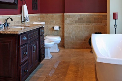 Diseño de cuarto de baño principal clásico con lavabo bajoencimera, armarios con paneles empotrados, puertas de armario de madera en tonos medios, encimera de granito, bañera exenta, baldosas y/o azulejos beige, baldosas y/o azulejos de piedra, paredes rojas y suelo de piedra caliza
