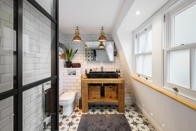 Modernes Badezimmer mit offenen Schränken, hellbraunen Holzschränken, weißen Fliesen, Metrofliesen, weißer Wandfarbe, Aufsatzwaschbecken, Waschtisch aus Holz, weißem Boden und brauner Waschtischplatte in London