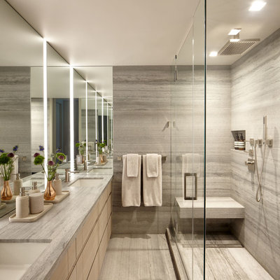 Inspiration for a mid-sized modern master gray tile and travertine tile travertine floor and gray floor corner shower remodel in New York with flat-panel cabinets, light wood cabinets, a wall-mount toilet, gray walls, an undermount sink, limestone countertops, a hinged shower door and gray countertops