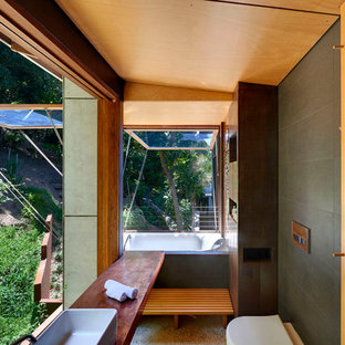 Inspiration for a tropical bathroom in Other with an alcove tub, gray tile, a vessel sink and brown benchtops.