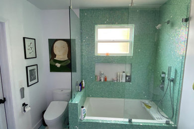 Inspiration for a mid-sized tropical master green tile and mosaic tile porcelain tile, multicolored floor and double-sink tub/shower combo remodel in Los Angeles with flat-panel cabinets, brown cabinets, an undermount tub, a two-piece toilet, beige walls, an undermount sink, solid surface countertops, a hinged shower door, white countertops and a floating vanity