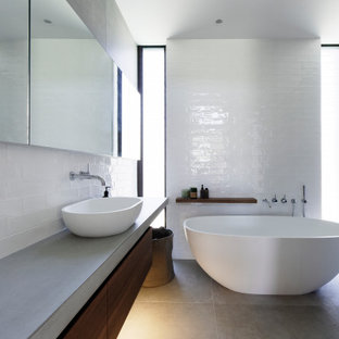 Inspiration for a mid-sized contemporary master bathroom in Central Coast with beaded inset cabinets, dark wood cabinets, a freestanding tub, an open shower, a wall-mount toilet, subway tile, white walls, porcelain floors, a console sink, concrete benchtops, grey floor, an open shower and grey benchtops.
