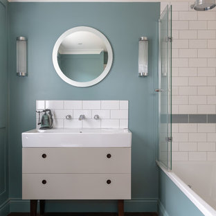 Inspiration for a contemporary bathroom in London with freestanding cabinets, grey cabinets, an alcove bath, a shower/bath combination, grey tiles, white tiles, metro tiles, blue walls, medium hardwood flooring, an integrated sink and white worktops.