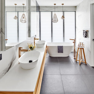 Expansive contemporary master bathroom in Sydney with flat-panel cabinets, beige cabinets, a freestanding tub, gray tile, porcelain tile, porcelain floors, a vessel sink, solid surface benchtops, grey floor and white benchtops.