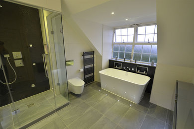 Cette image montre une salle de bain design avec des portes de placard noires, une baignoire indépendante, un espace douche bain, WC suspendus, un mur blanc, un sol en ardoise et un lavabo suspendu.
