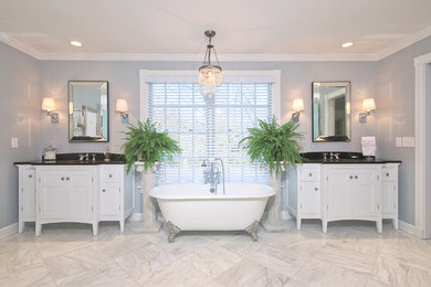 Inredning av ett klassiskt stort en-suite badrum, med ett undermonterad handfat, luckor med infälld panel, vita skåp, ett badkar med tassar, vit kakel, blå väggar och marmorgolv