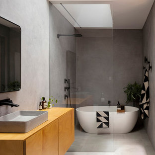 Photo of a modern master wet room bathroom in Sydney with flat-panel cabinets, medium wood cabinets, a freestanding tub, gray tile, grey walls, a vessel sink, wood benchtops, grey floor, an open shower and brown benchtops.