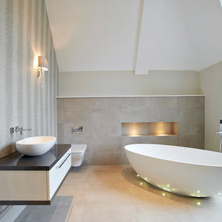 Mittelgroßes Modernes Badezimmer En Suite mit freistehender Badewanne, Wandtoilette, flächenbündigen Schrankfronten, weißen Schränken, braunen Fliesen, Aufsatzwaschbecken und schwarzer Waschtischplatte in London