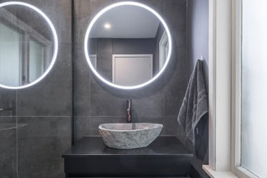 Foto de cuarto de baño moderno de tamaño medio con puertas de armario negras, baldosas y/o azulejos grises, lavabo sobreencimera, suelo gris y ducha con puerta con bisagras