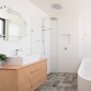 This is an example of a small contemporary master wet room bathroom in Melbourne with flat-panel cabinets, light wood cabinets, white tile, ceramic tile, white walls, ceramic floors, a vessel sink, wood benchtops, grey floor, an open shower, a corner tub and beige benchtops.