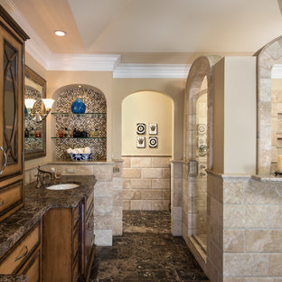 Inspiration for a large timeless master beige tile and limestone tile limestone floor and brown floor bathroom remodel in Detroit with an undermount sink, limestone countertops, beige walls, medium tone wood cabinets, glass-front cabinets, brown countertops, a two-piece toilet and a hinged shower door