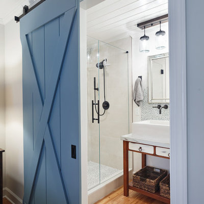 Inspiration for a country 3/4 glass tile medium tone wood floor and brown floor alcove shower remodel in Charlotte with furniture-like cabinets, brown cabinets, white walls, a vessel sink, a hinged shower door, marble countertops and white countertops