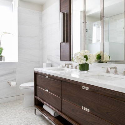 Example of a large trendy 3/4 white tile and marble tile white floor corner shower design in DC Metro with a one-piece toilet, an undermount sink, furniture-like cabinets, brown cabinets, white walls, solid surface countertops and white countertops