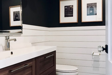 Imagen de cuarto de baño actual pequeño con armarios estilo shaker, puertas de armario de madera en tonos medios, sanitario de dos piezas, paredes negras, suelo con mosaicos de baldosas, lavabo integrado, encimera de acrílico y encimeras blancas