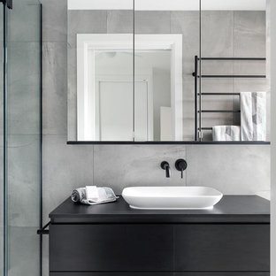 This is an example of a contemporary bathroom in Melbourne with black cabinets, cement tile, grey walls, cement tiles, a vessel sink, laminate benchtops, grey floor, black benchtops, flat-panel cabinets, gray tile and a hinged shower door.