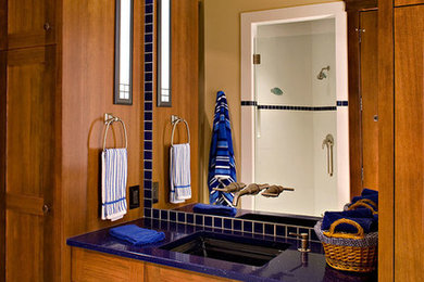 Expansive retro shower room bathroom in Calgary with a built-in sink, flat-panel cabinets, medium wood cabinets, glass worktops, blue tiles, glass tiles, beige walls and ceramic flooring.