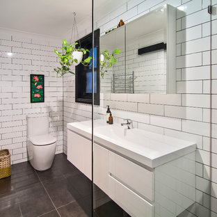 Esempio di una piccola stanza da bagno tropicale con ante di vetro, ante bianche, doccia a filo pavimento, WC monopezzo, piastrelle bianche, piastrelle diamantate, pareti bianche, pavimento con piastrelle in ceramica, lavabo integrato, top in superficie solida, pavimento nero, doccia aperta e top bianco
