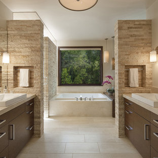 Photo of a contemporary master bathroom in Denver with a vessel sink, flat-panel cabinets, dark wood cabinets, marble benchtops, travertine floors, a drop-in tub, beige tile, beige walls and travertine.