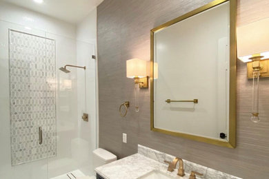 Mid-sized trendy master white tile and porcelain tile marble floor, white floor, single-sink and wallpaper alcove shower photo in Miami with shaker cabinets, blue cabinets, a two-piece toilet, brown walls, an undermount sink, marble countertops, a hinged shower door, white countertops and a freestanding vanity