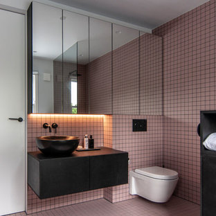 Idéer för att renovera ett mellanstort funkis svart svart badrum, med släta luckor, svarta skåp, en vägghängd toalettstol, rosa kakel, rosa väggar, rosa golv och ett fristående handfat