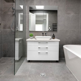 Photo of a large contemporary kids bathroom in Melbourne with flat-panel cabinets, white cabinets, a freestanding tub, gray tile, porcelain tile, porcelain floors, a vessel sink, grey floor, an open shower, white benchtops, a niche, a single vanity, a built-in vanity, an open shower, grey walls and engineered quartz benchtops.