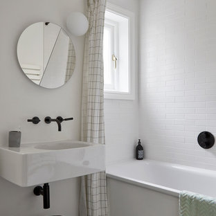 Small contemporary family bathroom in London with a built-in bath, white tiles, ceramic tiles, white walls, ceramic flooring, a wall-mounted sink, marble worktops, black floors, white worktops and a built-in shower.