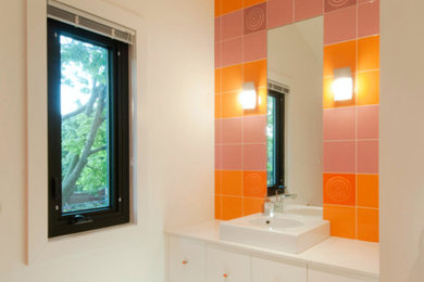 トロントにある中くらいなエクレクティックスタイルのおしゃれな浴室 (フラットパネル扉のキャビネット、白いキャビネット、オレンジのタイル、セメントタイル、白い壁、磁器タイルの床、オーバーカウンターシンク) の写真