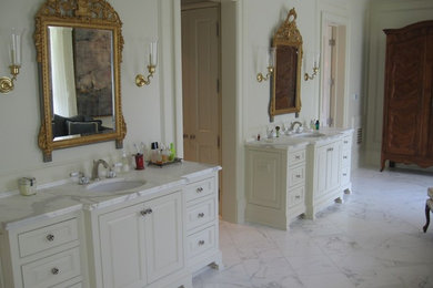 Aménagement d'une grande salle de bain principale classique avec des portes de placard blanches, un placard avec porte à panneau surélevé, un mur blanc, un sol en marbre, un lavabo encastré, un plan de toilette en marbre et un sol blanc.