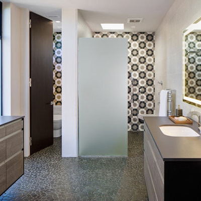 Inspiration for a mid-sized modern master beige tile, black tile, white tile and porcelain tile pebble tile floor and gray floor bathroom remodel in San Diego with flat-panel cabinets, distressed cabinets, a one-piece toilet, white walls, an undermount sink and solid surface countertops